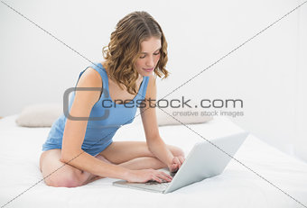Beautiful serious woman sitting on her bed typing on her notebook