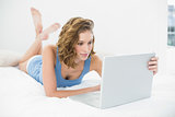 Attractive young woman using her laptop lying on her bed