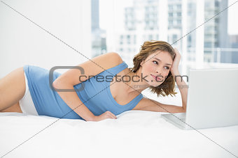 Lovely woman posing lying on her bed next to her notebook