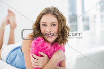 Lovely woman holding her heart pillow lying on her bed