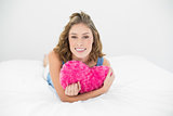 Attractive sweet woman cuddling with her heart pillow smiling at camera