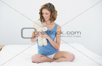 Pretty sweet woman holding her white teddy bear looking at it sitting on her bed