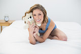 Happy woman posing with her white teddy bear sitting on bed