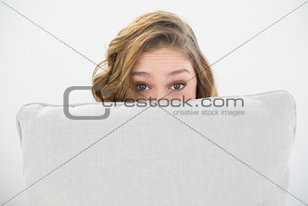 Astonished brunette woman hiding her face behind a white pillow
