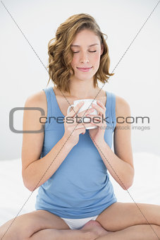 Content peaceful woman sitting on her bed holding white cup