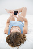 Lovely woman lying on her bed using her smartphone