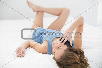 Gorgeous young woman lying on her bed phoning with her smartphone