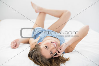 Lovely calm woman lying on her bed phoning with her smartphone