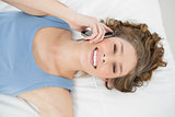 Beautiful young woman lying on her bed phoning using her smartphone