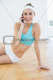 Cheerful sporty woman sitting on the floor phoning with her smartphone