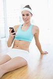 Content smiling woman holding her smartphone sitting on floor