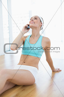 Happy woman in sportswear sitting on floor while phoning with her smartphone