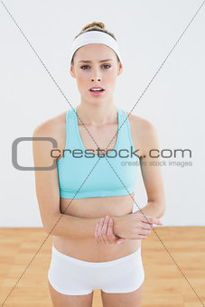 Young slim woman in sportswear touching her injured wrist