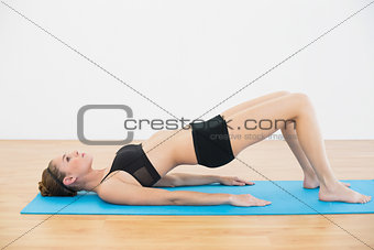 Focused sporty woman lying on blue exercise mat doing exercises