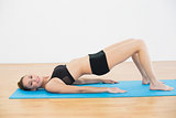Gleeful young woman in sportswear lying on exercise mat doing exercises