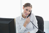 Gleeful chic businesswoman phoning with telephone sitting at her desk