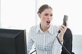 Shocked young businesswoman holding telephone looking at it