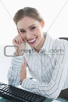 Cheerful chic businesswoman sitting at her desk smiling at camera
