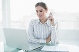 Attractive smiling businesswoman sitting in front of her laptop holding a pencil