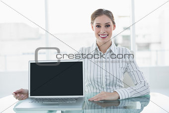 Cheerful attractive businesswoman showing notebook sitting at her desk