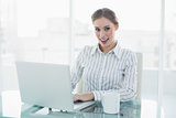 Gleeful lovely chic businesswoman sitting at her desk using her notebook