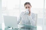 Beautiful businesswoman sitting at her desk drinking from cup