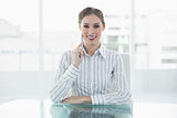 Lovely thinking businesswoman sitting at her desk smiling at camera