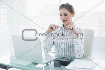 Attractive chic businesswoman holding a pencil sitting at her desk