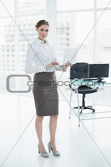 Attractive smiling businesswoman holding her notebook standing in her office