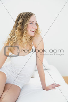 Pretty cheerful blonde sitting on bed looking away
