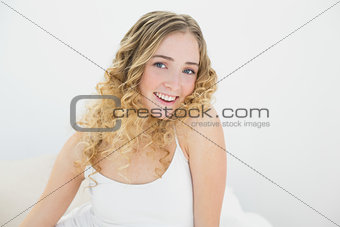 Pretty gleeful blonde sitting on bed looking at camera