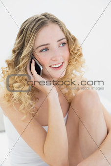 Pretty cheerful blonde sitting on bed phoning