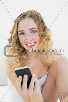 Pretty blonde sitting on bed holding smartphone