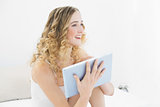 Pretty cheerful blonde sitting on bed holding tablet