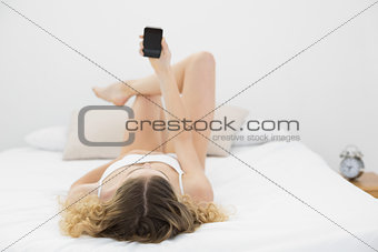 Pretty blonde lying on bed holding smartphone
