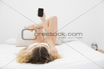 Attractive blonde lying on bed holding smartphone