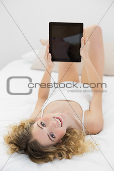 Pretty happy blonde lying on bed holding tablet