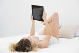 Pretty calm blonde lying on bed holding tablet