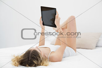 Pretty calm blonde lying on bed holding tablet