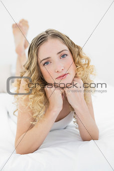 Pretty thoughtful blonde lying on bed looking at camera