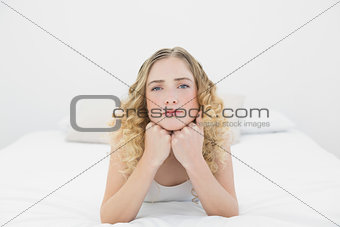 Pretty frowning blonde lying on bed looking at camera