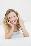 Pretty happy blonde lying on bed phoning