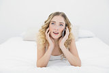 Pretty thoughtful blonde lying on bed phoning