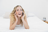 Pretty cheerful blonde lying on bed phoning