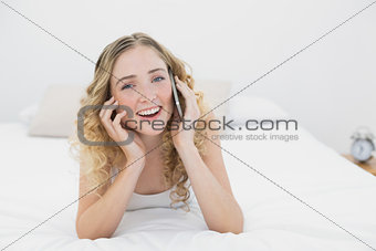 Pretty smiling blonde lying on bed phoning