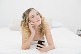 Pretty thoughtful blonde lying on bed using smartphone