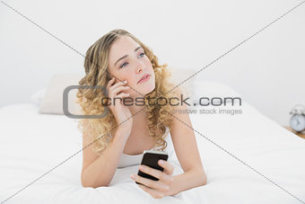 Pretty thoughtful blonde lying on bed using smartphone