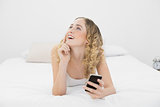 Pretty day dreaming blonde lying on bed using smartphone