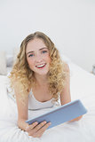 Pretty cheerful blonde lying on bed using tablet