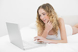 Pretty happy blonde lying on bed using laptop